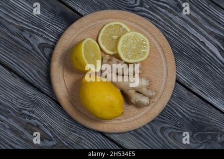 Lemon and ginger on a cutting board. The lemon is cut into slices. Against a background of black pine boards. Stock Photo