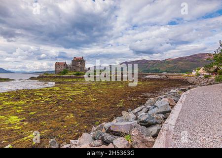 Eilean Donan Castle in the Scottish Highlands at low tide. Path along the lake. Historic stone bridge to the fortress. Old fortress in Scotland in the Stock Photo