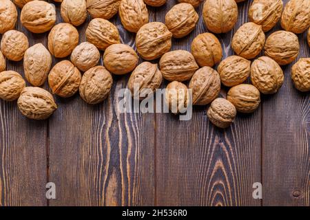 many walnuts with shells randomly scattered on brown wooden surface with copy space at bottom of picture Stock Photo