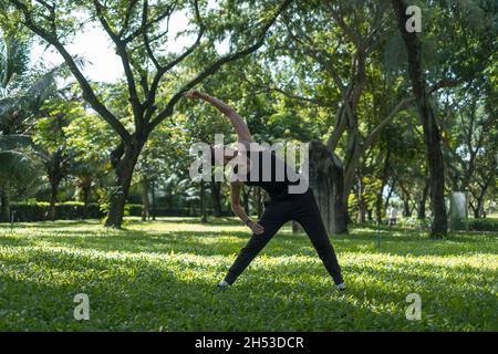Sporty active young man in black sportswear doing sport exercises in the park. Portrait of handsome fit man doing stretching exercise outdoors.  Stock Photo