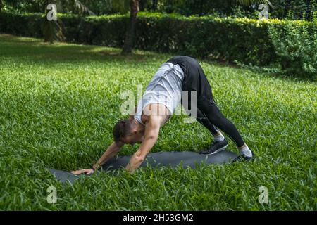 Sporty active young man in sportswear doing sport exercises in the park. Muscular fit man doing exercises outdoors. Healthy lifestyle concept, sport Stock Photo