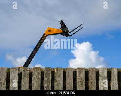Small forklift behind wooden fence against sky. Stock Photo