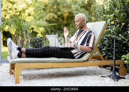 Latin man using laptop on lounger at house garden Stock Photo