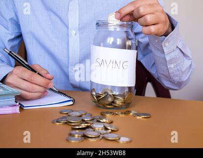 Businessman puts money coins into to glass jar, saving money and finance accounting concept. Stock Photo