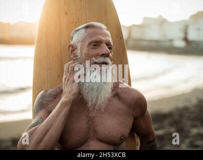 Fit senior man having fun practicing surf on tropical beach - Elderly healthy people lifestyle and extreme sport concept Stock Photo