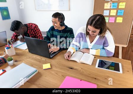 Young multiracial students reading books and using laptop in classroom while studying together - School education concept - Focus on female Stock Photo