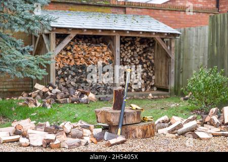 Chopping firewood. Axe and log pile outside a log store in a UK garden Stock Photo