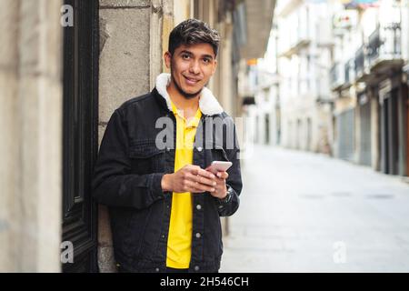 Young man standing next to a building door looking at the camera and smiling Stock Photo