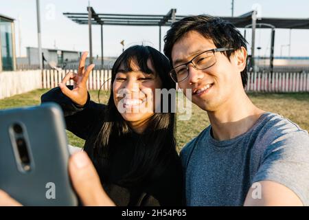 Young asian couple having fun while taking selfie with smartphone outdoors Stock Photo