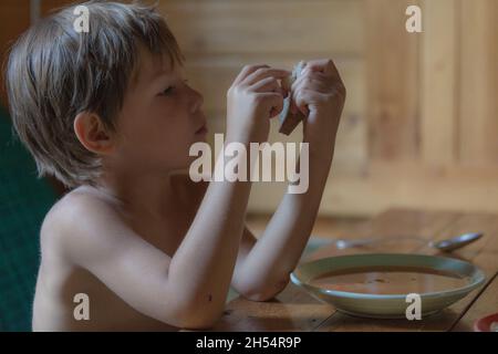 Portrait of small boy child eating soup meal or breakfast having lunch by the table at home with spoon white Stock Photo