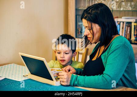 POZNAN, POLAND - Nov 12, 2017: A Polish Caucasian woman and a boy drawing on a chalkboard on the table at home Stock Photo