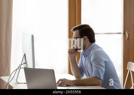 Pensive young businessman in eyewear working on computer. Stock Photo