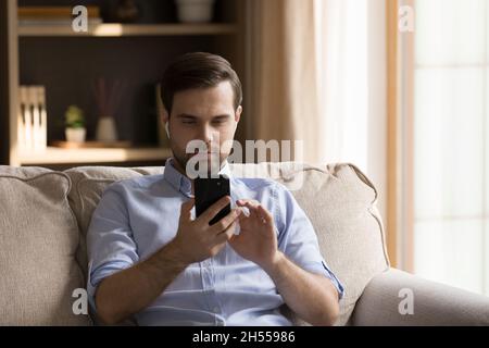 Happy young handsome man in earbuds using cellphone. Stock Photo