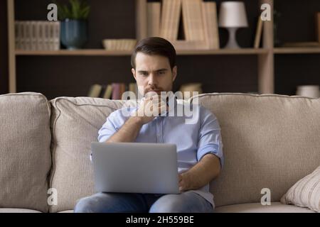 Pensive young man working on computer at home. Stock Photo