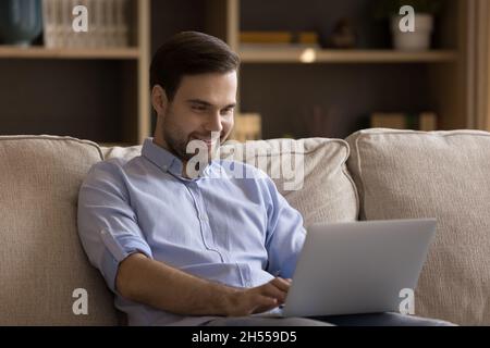 Smiling millennial handsome guy using laptop at home. Stock Photo