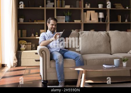 Happy young relaxed man using digital touchpad gadget. Stock Photo