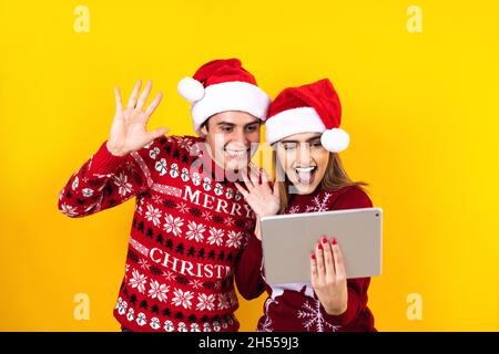 young latin couple having christmas video call using digital tablet or touchpad on a yellow background Stock Photo