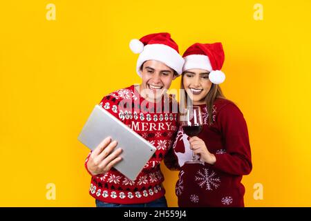 young latin couple having christmas video call using digital tablet or touchpad on a yellow background Stock Photo