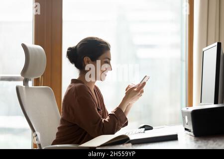 Smiling Indian employee rest at workplace with smartphone Stock Photo