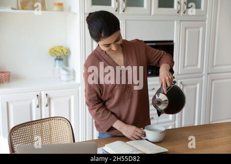 Indian woman holding electric teapot pouring water into ceramic cup Stock Photo