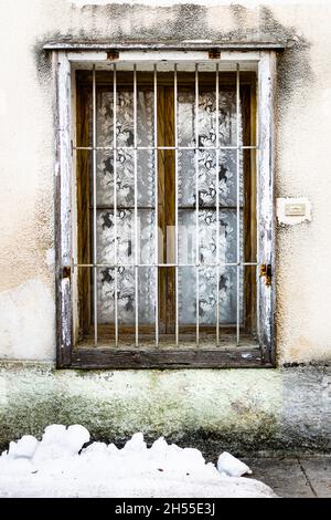 Old wooden window with iron bars and curtains, snow on the ground Stock Photo