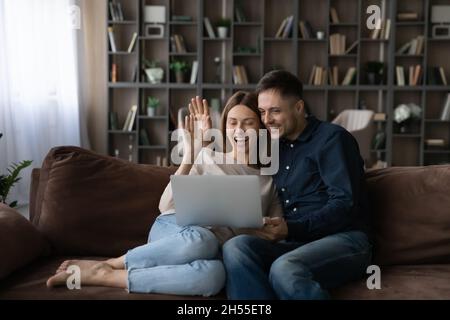 Happy couple hugging waving hands, chatting online by video call Stock Photo
