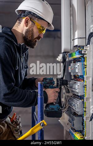 A male electrician works in a switchboard with an electrical connecting cable. Stock Photo