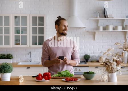 Distracted from cooking food happy young man using smartphone. Stock Photo