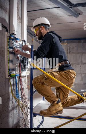 A male electrician works in a switchboard with an electrical connecting cable. Stock Photo