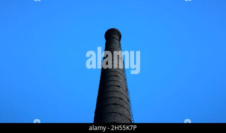 A large chimney in an old factory. smoke stack An old black brick chimney against a blue sky. Stock Photo