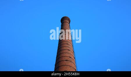 tall chimney old red bricks in an old factory. smoke stack An old brick chimney against a blue sky. Stock Photo