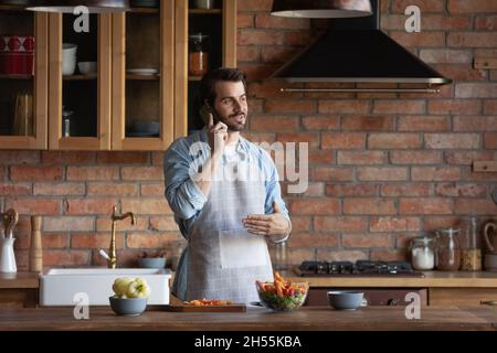 Millennial man cooking healthy salad talk on phone at kitchen Stock Photo