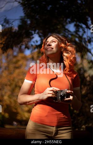 from below red-haired woman smiling with vintage camera outdoors with lights and shadows Stock Photo