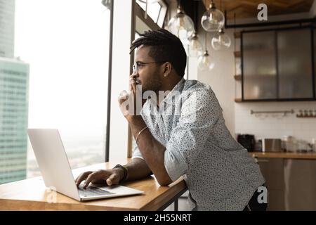 Distracted from computer work dreamy african man looking in distance. Stock Photo