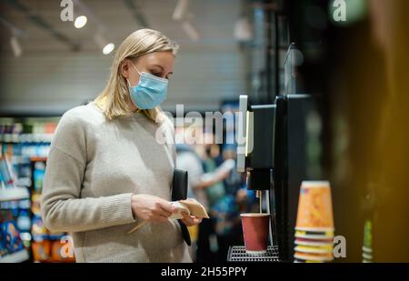 Woman in mask using coffee vending machine. Stock Photo