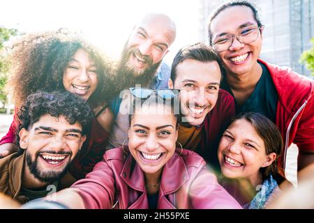 Multi cultural guys and girls taking selfie outdoors with backlight - Happy milenial friendship concept on young multiracial friends having fun day Stock Photo