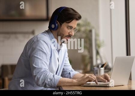Focused young 30s businessman in headphones using computer. Stock Photo