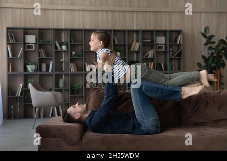 Smiling loving father lifting little daughter pretending flying on couch Stock Photo