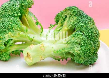 Two Fresh and Raw Pieces of Broccoli on White Plate. Uncooked Green Cabbage. Vegan and Vegetarian Culture. Raw Food. Healthy Eating and Vegetable Diet Stock Photo