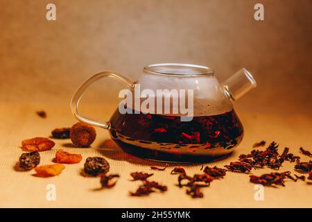 Glass teapot full of hot tea with dried pink coloured tea leaves Stock Photo