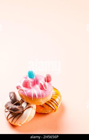 Photograph of three donuts decorated with jelly beans and drawn with chocolate.The photo is taken in vertical format on a cream colored background.The Stock Photo