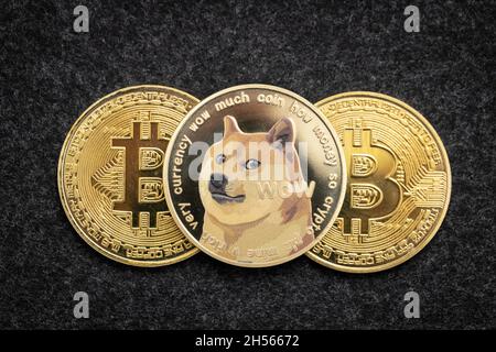 Dogecoin cryptocurrency physical coin laying on top of two bitcoin coins Stock Photo