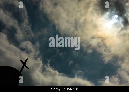 Dramatic scene Sky with sun obsured by clouds and church top cross black silhouette Sun shining through white and dark clouds beautiful view Stock Photo