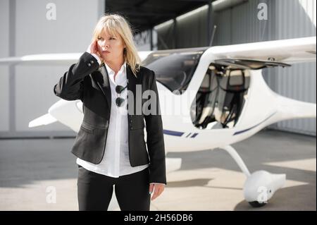 Beautiful professional female spy agent bodyguard securing airplane on private airport. Security police woman in civilian black suit. Close security p Stock Photo