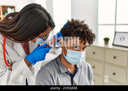 Young latin doctor woman auscultating the ear of man using otoscope at examination room. Stock Photo