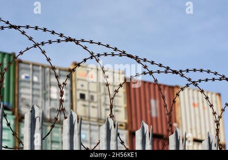 Freight shipping containers piled high behind a barbed razor wire topped fence at one the the UK’s busiest ports in Southampton. Stock Photo