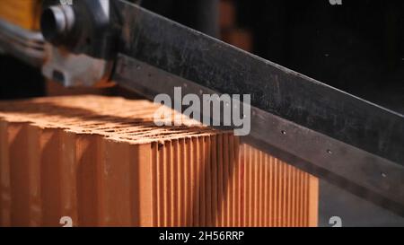 Professional saw for cutting bricks. Close-up of unknown worker using a professional saw cutting the brick at construction site. Stock Photo