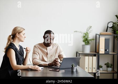 Minimal portrait of two modern business partners using laptop while discussing project at desk in office, copy space Stock Photo