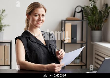 Portrait of confident businesswoman smiling at camera while sitting at desk in graphic office interior Stock Photo