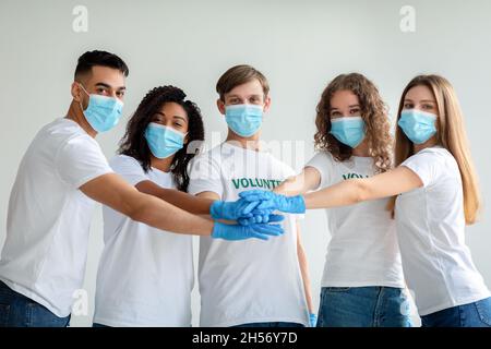 Unity and volunteering concept. Group of young diverse volunteers in masks and gloves joining hands together Stock Photo